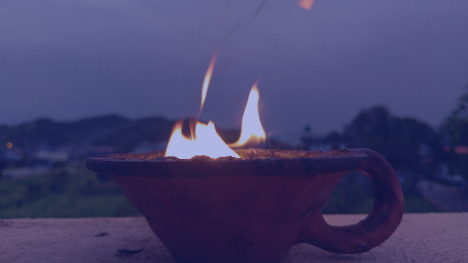 A clay oil lamp burning softly against a dusk sky